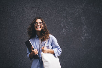 Half length portrait of intelligent smiling female posing for camera with laptop computer in hands. Carefree Female freelancer standing near copy space background