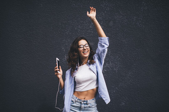 Smiling female dancing with smartphone device while listen audio on mobile app. Brunette young woman in headphones enjoying online music playlist on cellphone. Copy space area for advertising