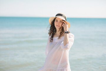 Fototapeta na wymiar Young brunette teenager girl with curly hair walking on the seashore in sunny day.