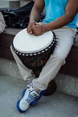 An African-American plays a drum, the hands of a black guy lie on the white deck of an African djembe drum, a street musician, a part of a human body.