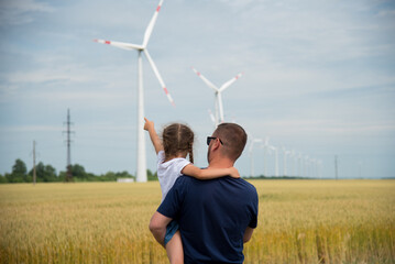 A girl and her dad look at the wind generator in the field. Ecology. Future.