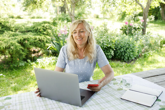 Smiling mature woman having video call via computer in the home garden office. Online team meeting video conference calling from home. Attractive Businesswoman Telework. Business video conferencing. 