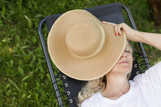 Woman Sleeping In Garden Recliner Chair. Summer Vacation In The Yard. Mature Scandinavian Female Life In Retirement. Good Living. Top View. Beautiful Middle Aged Woman Resting From Fatigue
