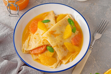 Delicious crepes suzette with orange syrup and slices fruits on a plate on a gray concrete background, top view