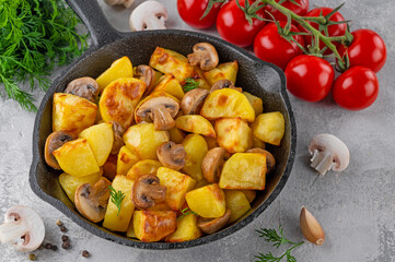 Baked potatoes with mushrooms and garlic in a cast iron skillet on a gray concrete background. Top view. Copy space.