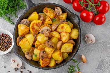 Baked potatoes with mushrooms and garlic in a cast iron skillet on a gray concrete background. Top view. Copy space.