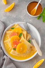 Fototapeta na wymiar Delicious crepes suzette with orange syrup and slices fruits on a plate on a gray concrete background, top view