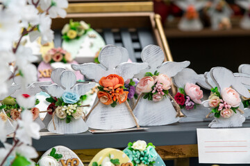 White wooden angel toys with artificial flowers stands on shelf of street market. Selective focus. Easter decoration theme.