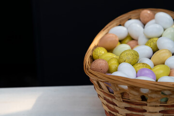 Wooden basket full of colorful eggs stands on table against black background. Selective focus. Copy space for your text. Easter celebration theme.
