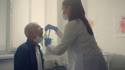 Latino doctor collecting saliva sample senior man closeup. Covid test concept.