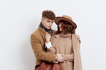 a sweet, joyful, pleasant stylish couple stands on a white background in autumn coats and gently hug each other