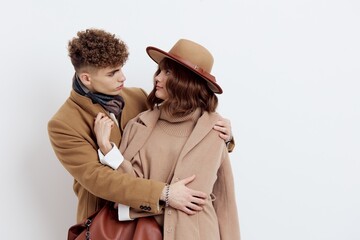 a sweet, joyful, pleasant stylish couple stands on a white background in autumn coats and gently hug each other, a woman has a hat on her head and she is holding a bag