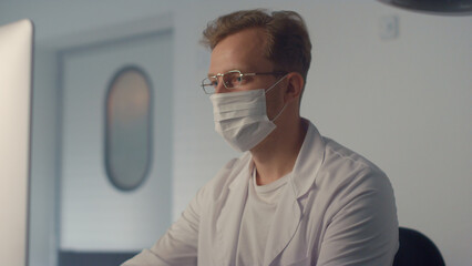 Fototapeta na wymiar Masked doctor watching monitor in clinic close up. Man physician writing report 