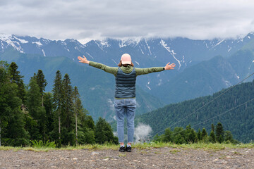 Happy girl with her arms outstretched enjoying the view of mountain peaks. Traveling and hiking concept.
