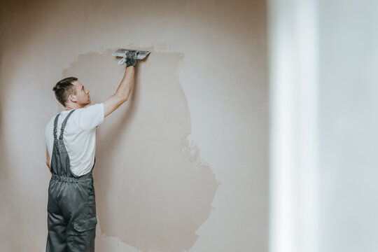 Builder in work overalls plastering a wall indoor