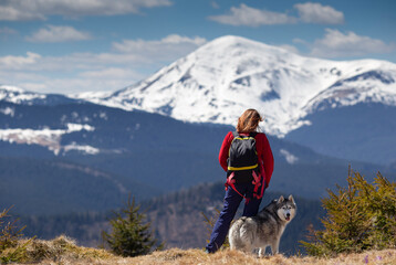 Girl with backpack resting with her Siberian husky dog together outdoor. Human and animal friendship concept. Snowy peak in the background