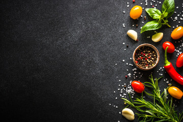 Food background on black stone table with fresh vegetables, herbs and spices. Ingredients for cooking with copy space.