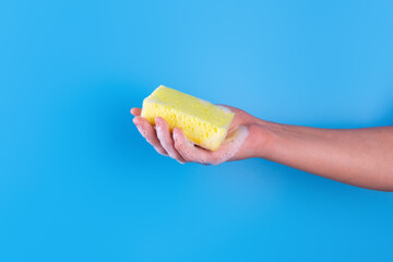 Persons hand holding yellow sponge for dish wash. Washcloth covered in soap. Domestic chores and...