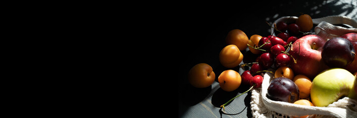 Fresh ripe fruits and berries on a black wooden background in an ecological mesh bag. Lifestyle....