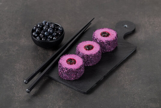 Mousse blueberry chocolate cream dessert, in the form of round sweet sushi, on a serving board. Dark gray background
