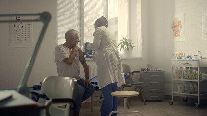 Medical specialist injecting vaccine to senior patient shoulder in hospital.