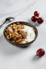 granola with yogurt in a bowl, next to a spoon and grapes