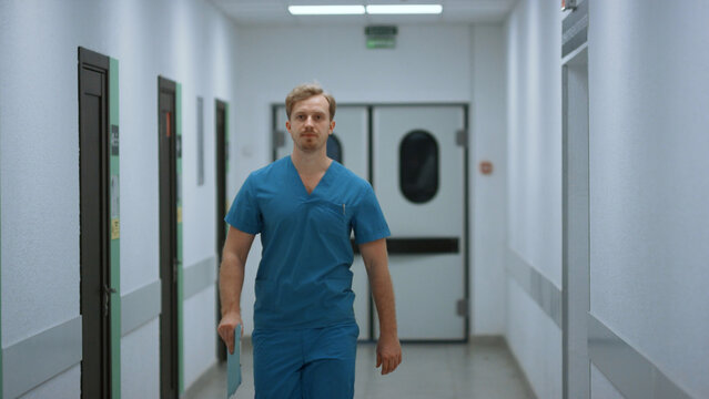 Serious Doctor Walking Down Hospital Corridor. Medic Going In Clinic Hallway.