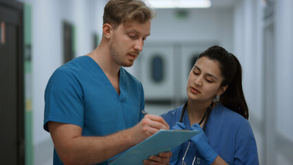 Surgeon discussing patient diagnosis with nurse standing clinic corridor closeup