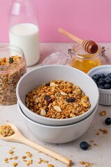 Delicious granola with raisin, sunflower seeds, peanut and hazelnut in bowl served with bottle of milk, honey and blueberries on pink background. Healthy vegan breakfast food. Selective focus.