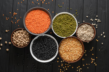 Overhead view of bowls of assorted raw legumes on a dark wooden table