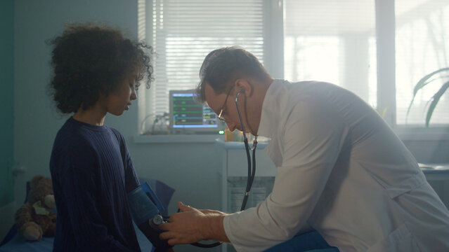 Doctor Measure Blood Pressure To African American Girl In Clinic Office.