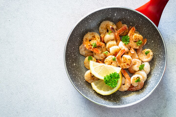 Frying shrimps with lemon in the frying pan. Top view image on black.