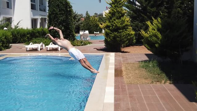 Man doing a backflip dive stunt. Man dives to swimming pool. Slow motion video footage of man jumping to the turquoise colored water of swimming pool. Summer leisure activities