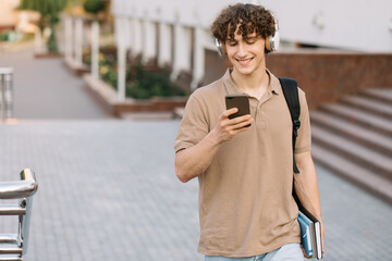 Attractive curly young man university or college student with phone walking around campus