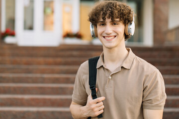 Portrait of attractive curly haired male student in headphones smiling