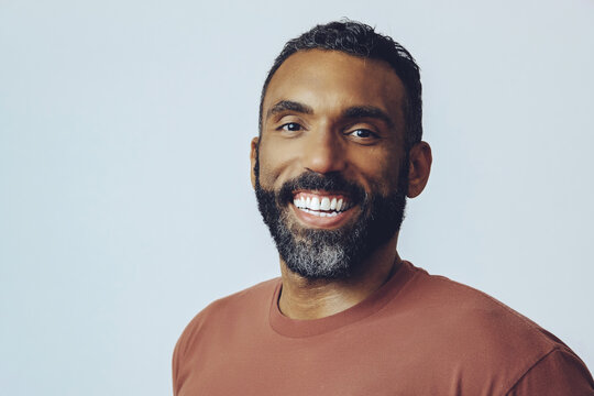 headshot portrait of a handsome smiling bearded mid adult man looking at camera against gray background studio shot