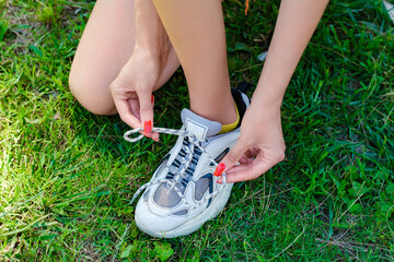 Young beautiful woman wearing turquoise tee on city park, outdoors tying lace running shoes getting ready for run. Jogging girl exercise motivation health and fitness.