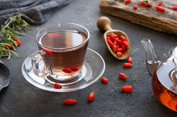Cup of herbal goji berry tea with fresh goji berries on rustic table