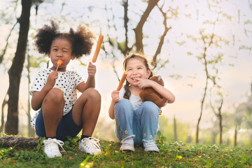 Happy cheerful white girls and black girl eat sausage together at outdoors park , Relationship...