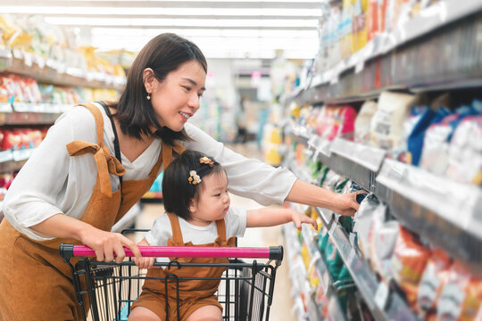 Asian mother and her daughter buying food at huge supermarket , Baby sit in trolley, Family shopping concept.
