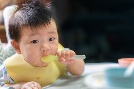 Asian baby girl with apron eat food by spoon and feed her self, Healthy nutrition of solid food for infant concept.