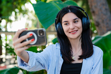 Young woman smiling confident wearing striped shirt standing on city park, outdoors doing video call or making selfie using smartphone.