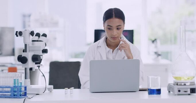 Young researcher or biologist thinking of new innovative study to develop medical research. Biotechnology chemist looking at statistics results. Female scientist working on a laptop in a modern lab.