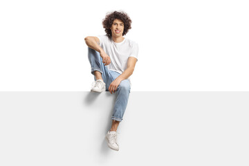 Casual young man with curly hair sitting on a blank panel