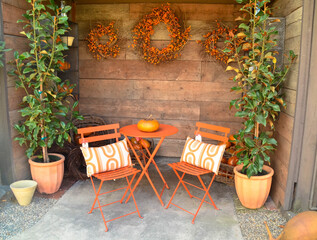 Backyard living, orange chairs with cushions and a table on the patio with plants and a wooden wall