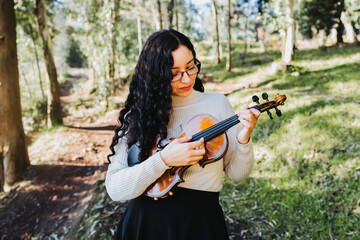 curly brunette woman using glasses and doing pizzicato technique in violin. Selective focus.
