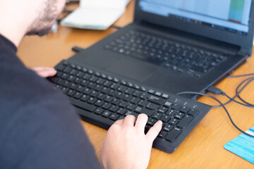 Unrecognizable man working in front of a laptop with an extra keyboard