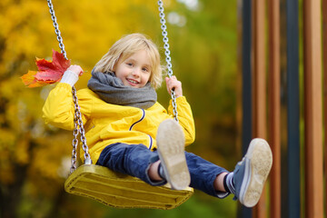 Little boy having fun on a swing on the playground in public park on autumn day. Happy child enjoy swinging.