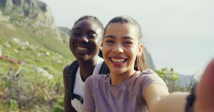 Two girl friends taking a selfie while hiking on a mountain trail outdoors. Happy women smiling and laughing while taking pictures with a nature view in the background. Getting fit and staying active