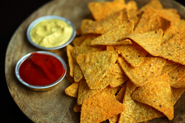 Nachos chips with sauces on a wooden board.